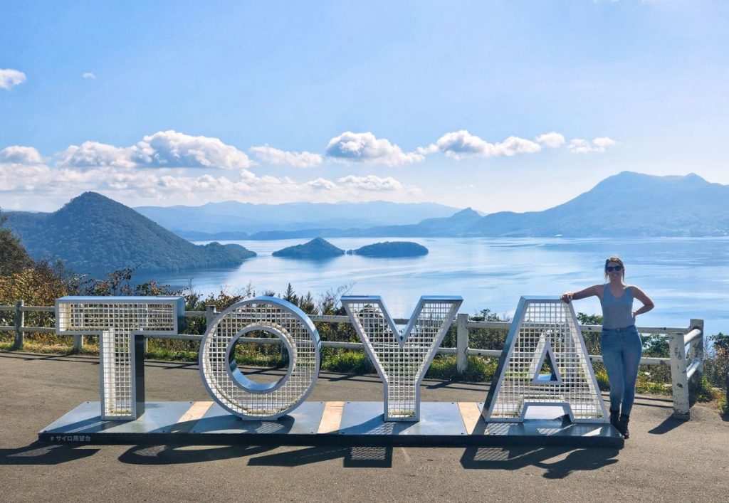 me standing with the Toya sign in Lake Toya Onsen town - day trips from sapporo